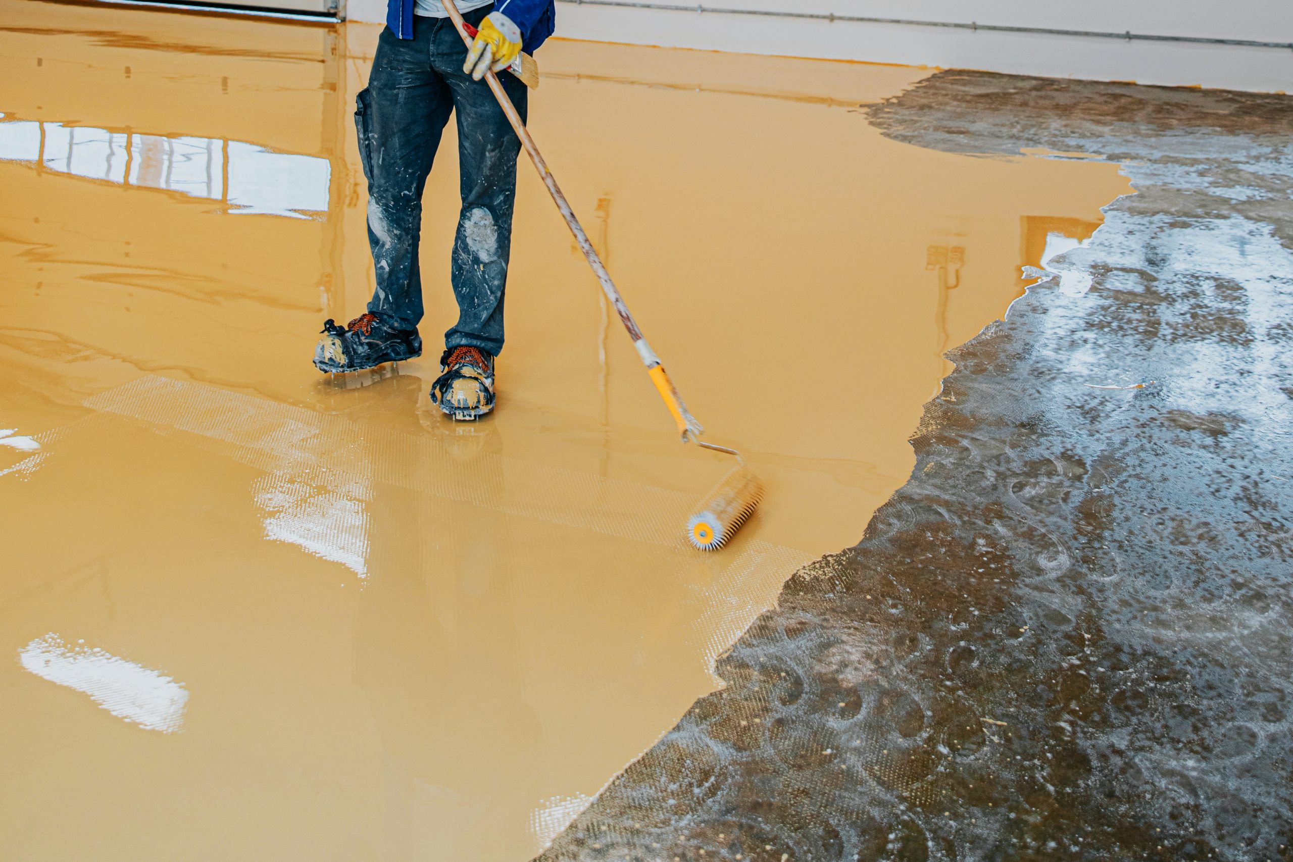 Worker, coating floor with self-leveling epoxy resin in industri